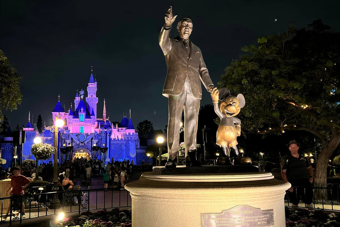 Nighttime image of the Partners statue at Disneyland, with Sleeping Beauty Castle in the background